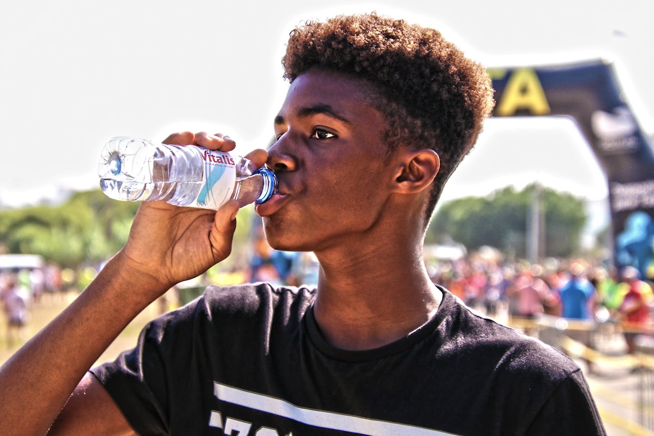 about-us-02 A young man drinking bottled water outdoors at a sporting event, showcasing hydration and fitness.