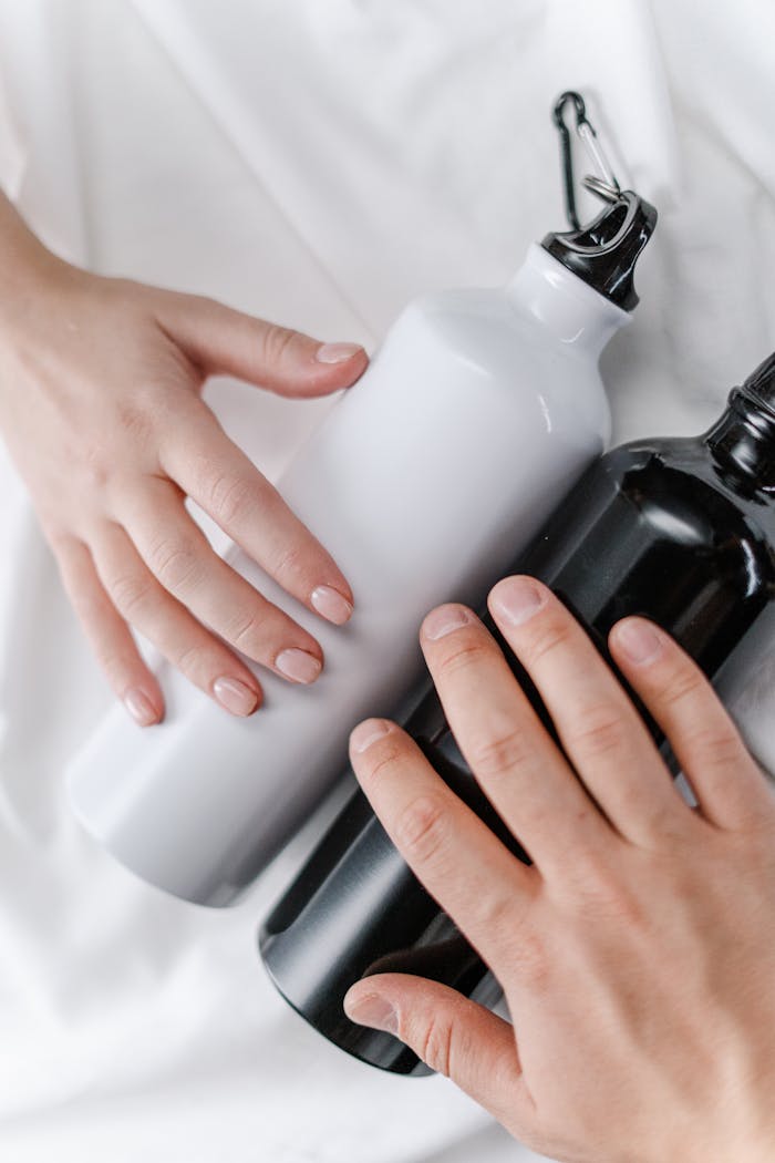 about-us-02 Close-up of hands with black and white reusable bottles on a white surface, promoting eco-friendly habits.