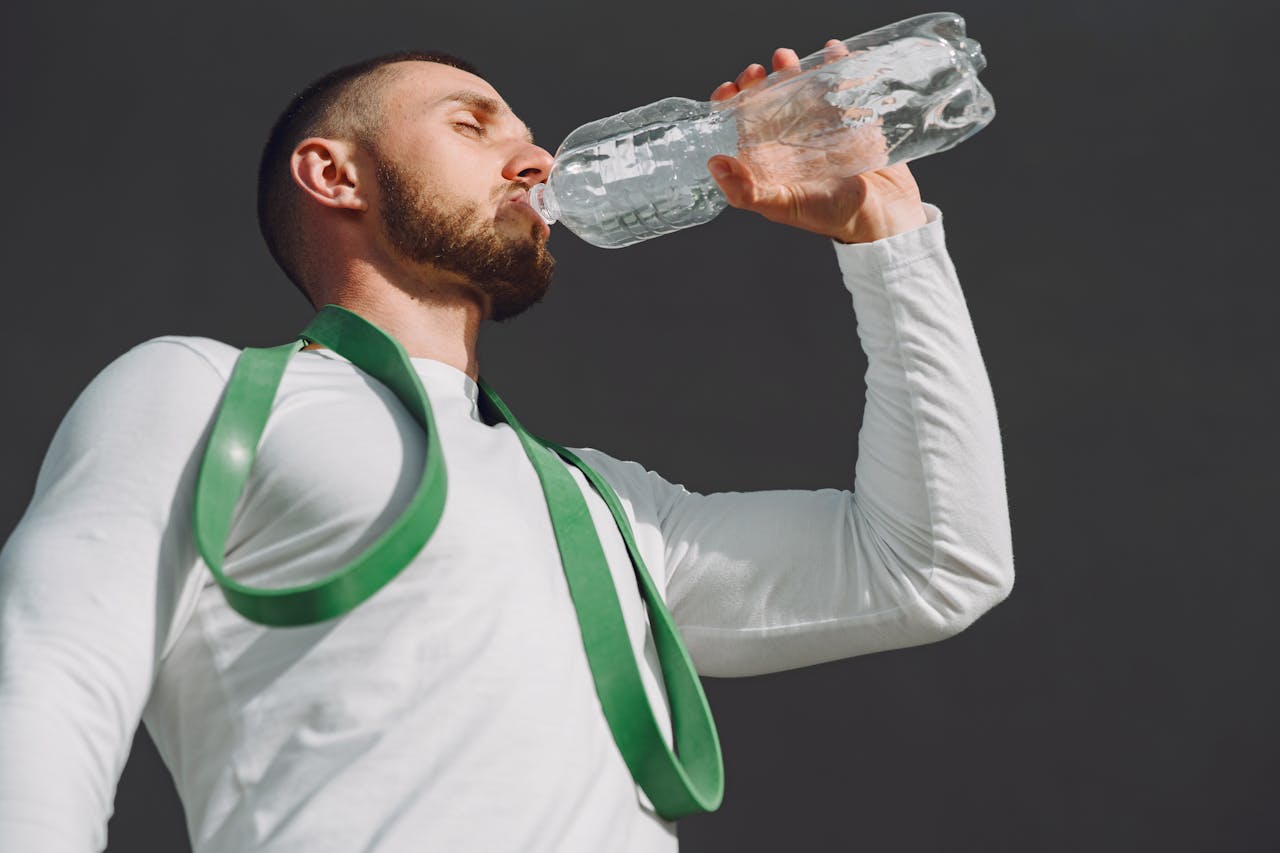 A fit man in sportswear drinking water outdoors, highlighting hydration and fitness.