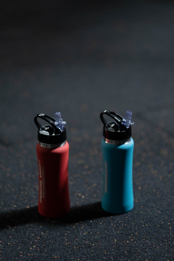 about-us-01 Two vibrant sports bottles on a dark textured floor, blue and red.